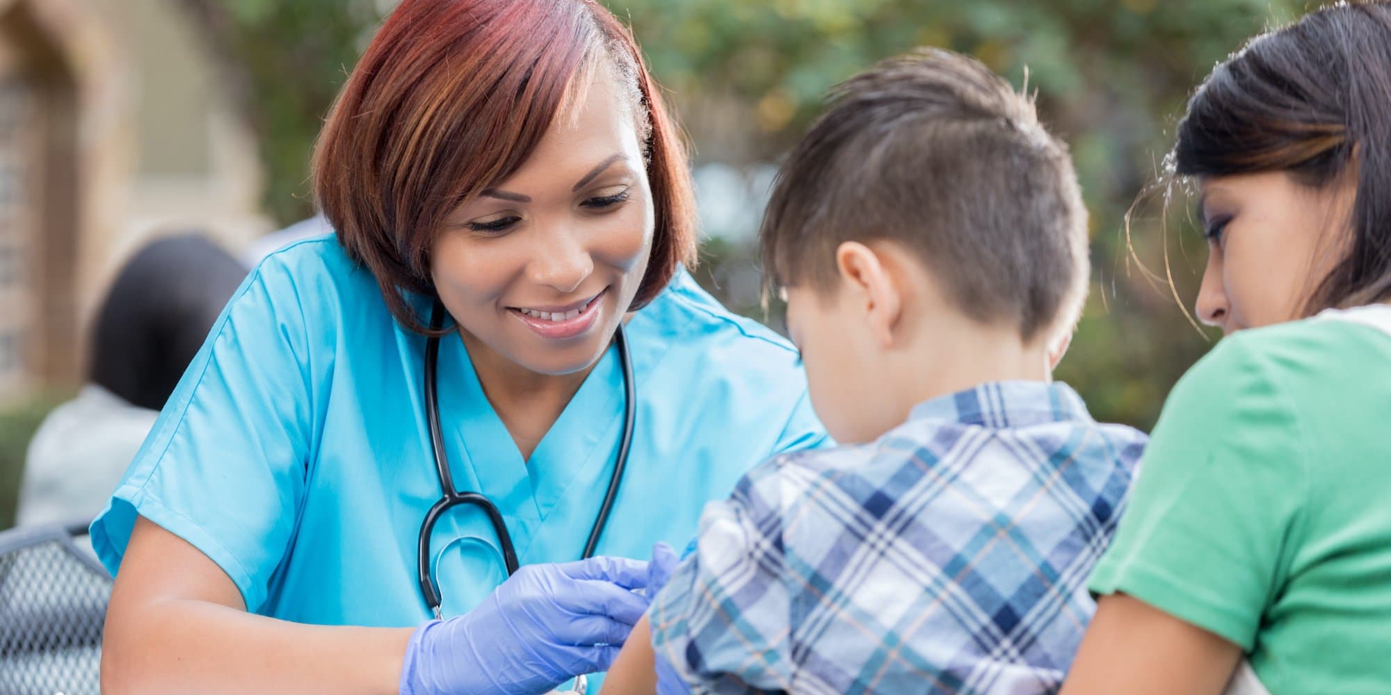person in scrubs with stethoscope examining child outdoors