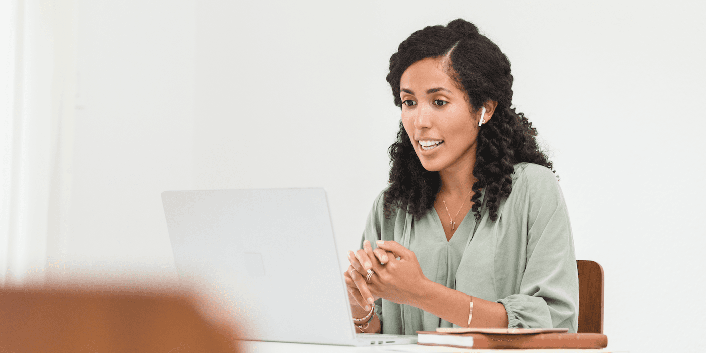 person leading videoconferencing meeting, sitting at a table looking at a laptop
