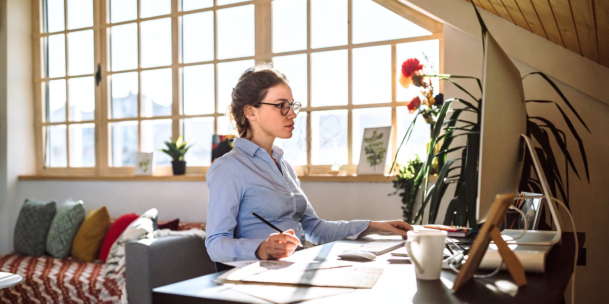 person sitting at desk looking at computer with pen in hand