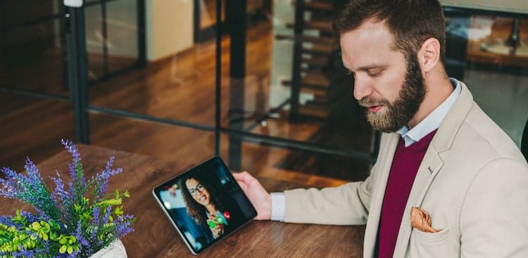 person sitting at a table making a video call on a tablet