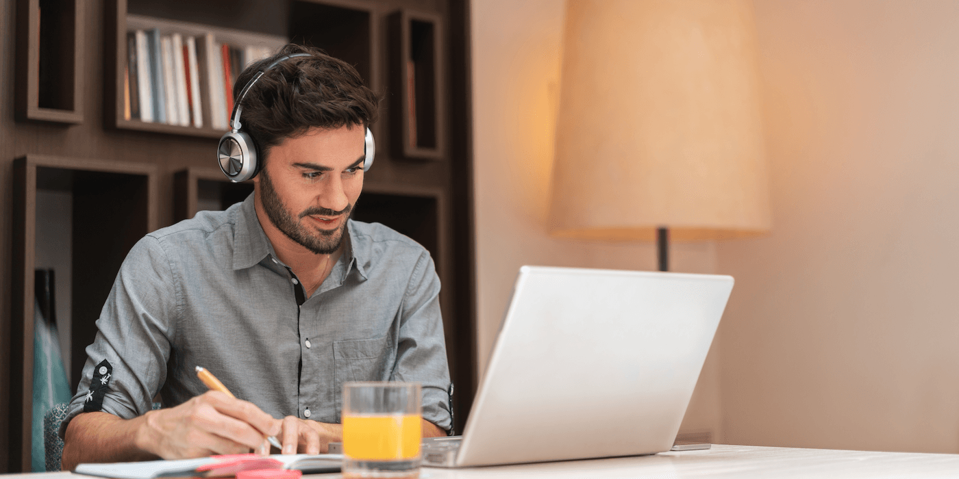 person sitting at home with a laptop and notebook wearing headphones