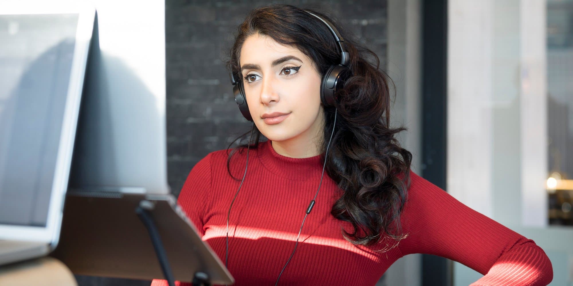 person working on laptop at standing desk in office while wearing headphones