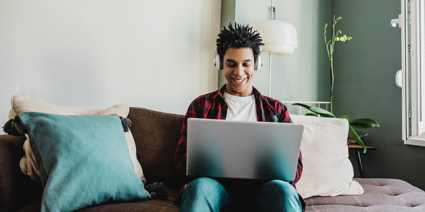 man with headphones sitting on a couch looking at a computer