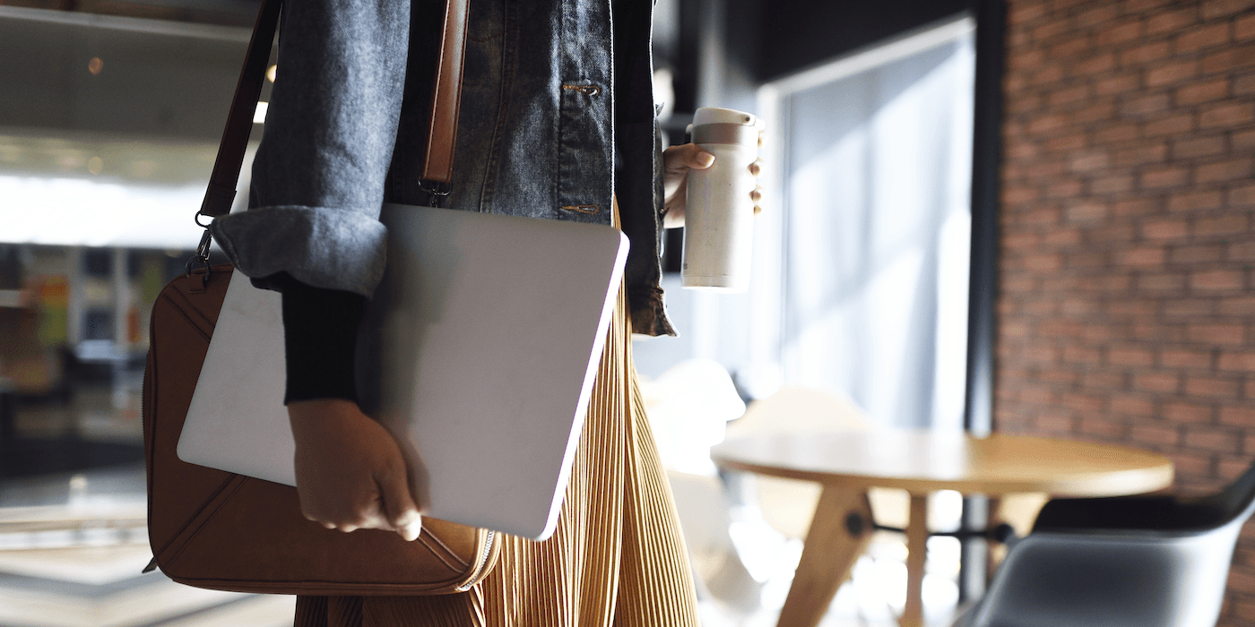 person carrying work bag, laptop, and travel mug walking into an office, their face and shoulders not visible