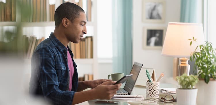 person sitting at desk with computer looking at phone courtesy JGI/Tom Grill/Getty Images