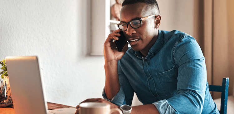person sitting at home working on a laptop and speaking on a cell phone