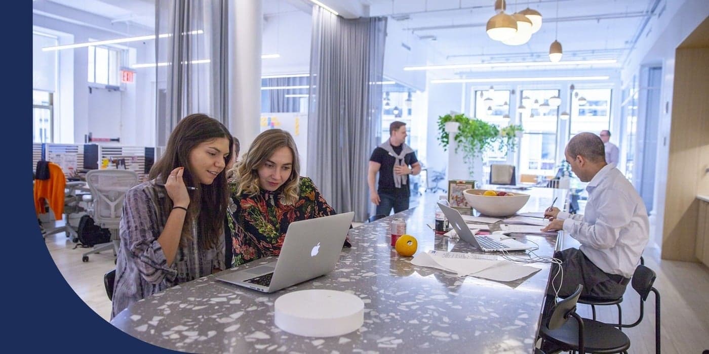 Coworkers collaborating at a high-top communal table inside an office.