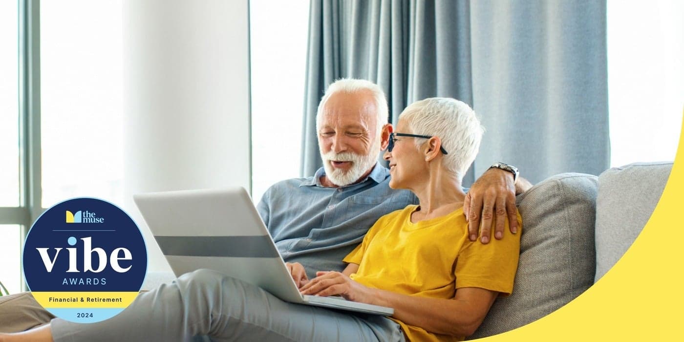 An elderly couple smiling while using a laptop on the couch