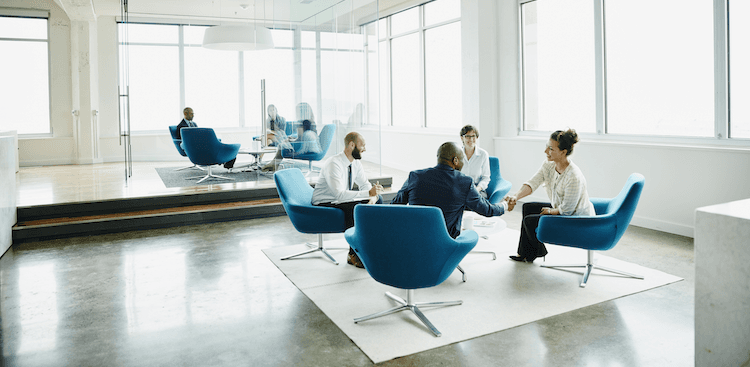group of co-workers sitting in a common area, two shaking hands,