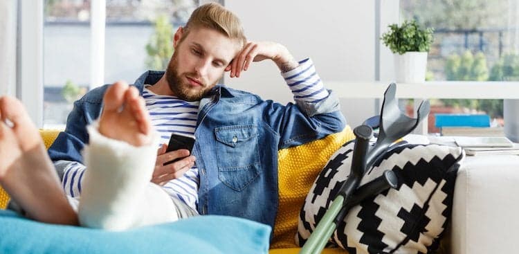 person sitting on a couch with their feet up, one leg in a cast, looking at their phone