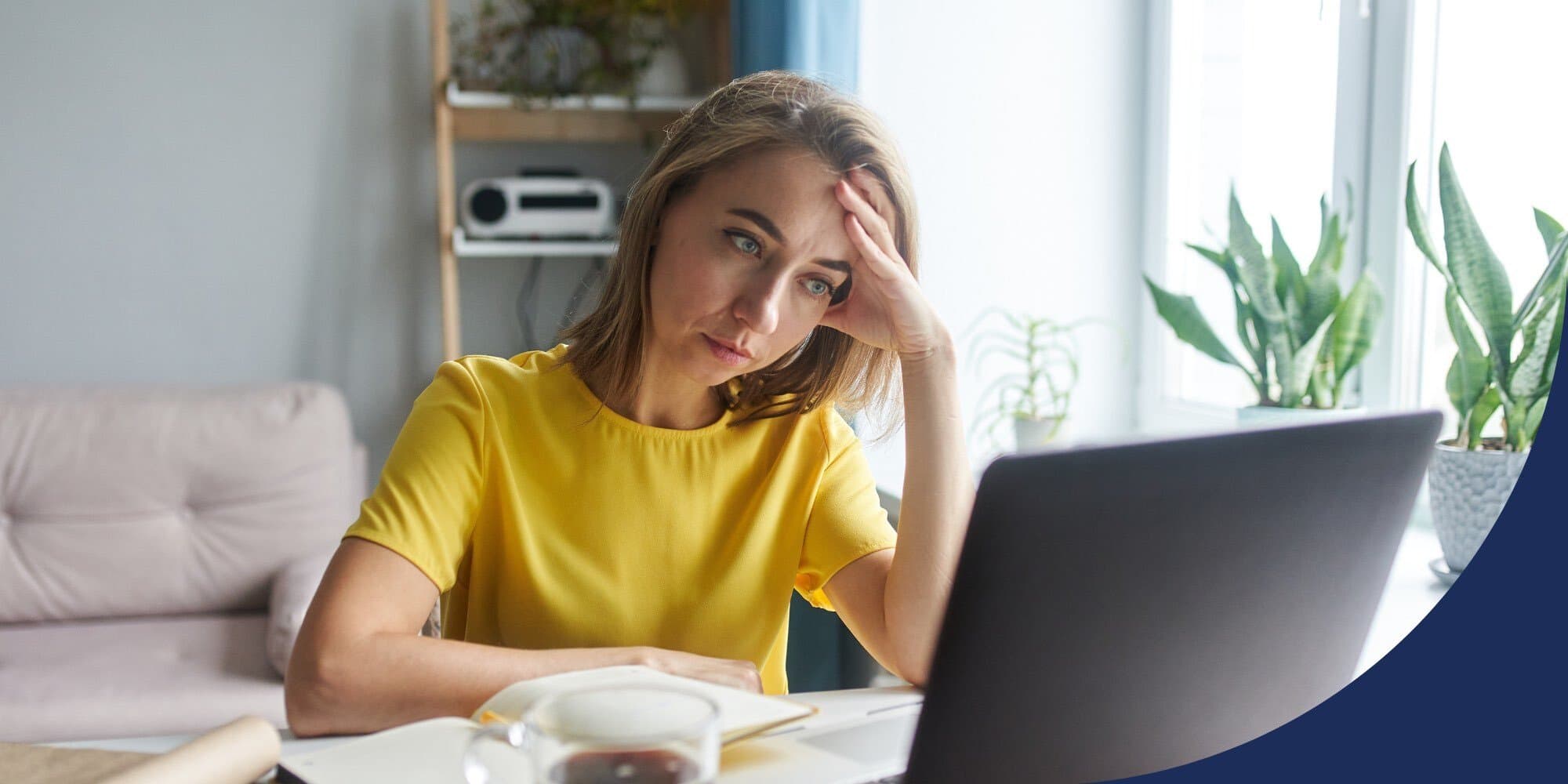 person sitting at a table looking at an open laptop, leaning their head on one hand, elbow propped on the table