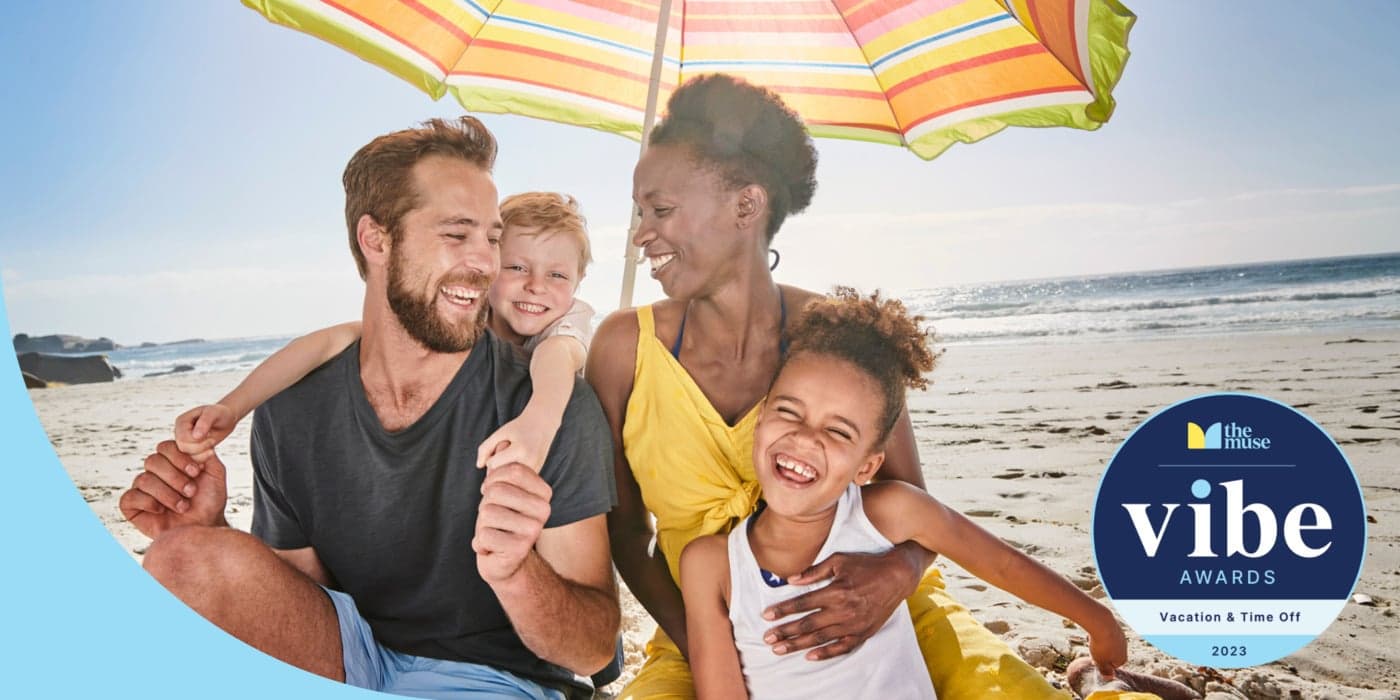 A family with small children smiling and embracing on the beach under an umbrella.