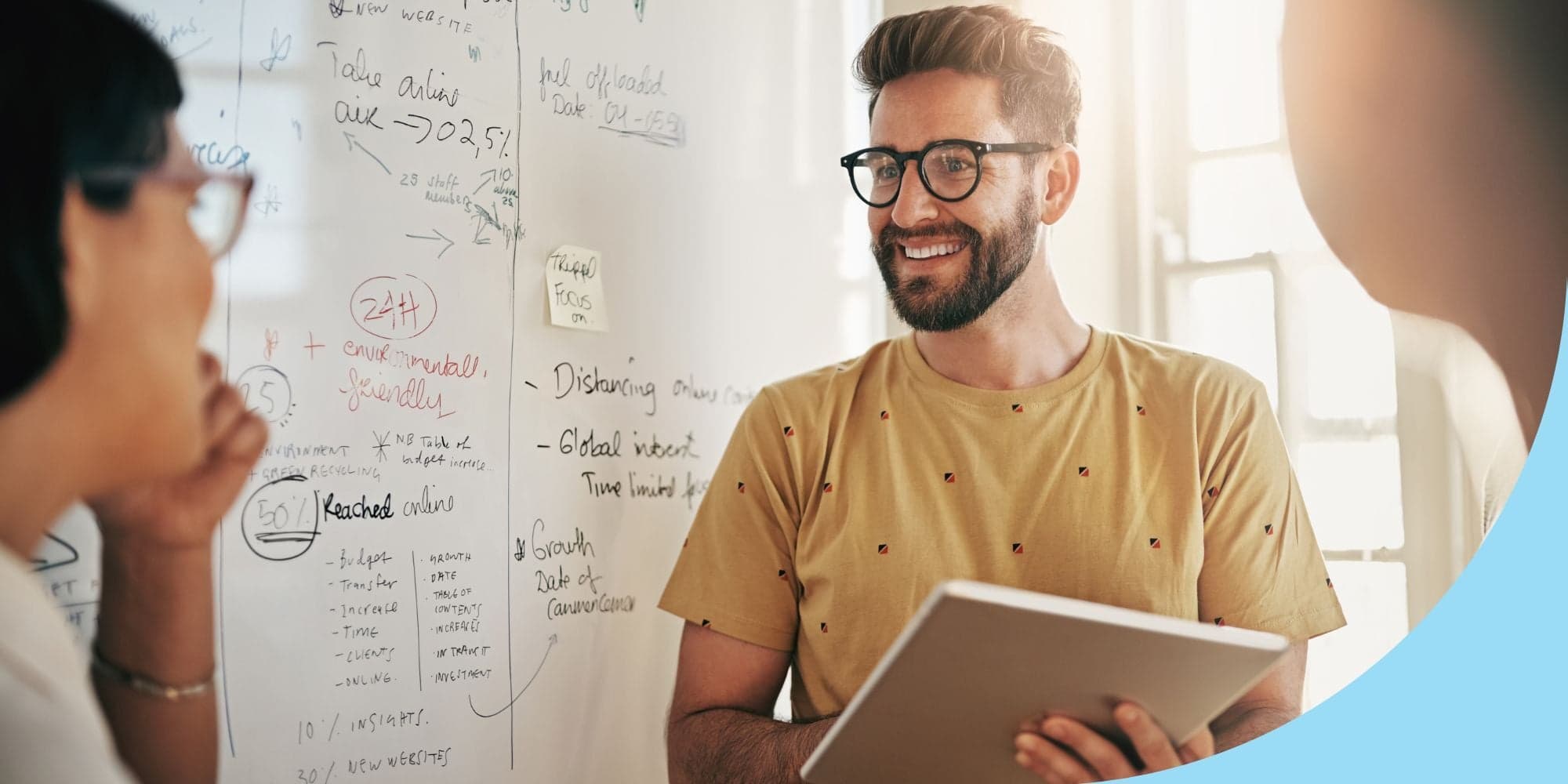 tech worker talking to coworkers in front of a whiteboard and smiling