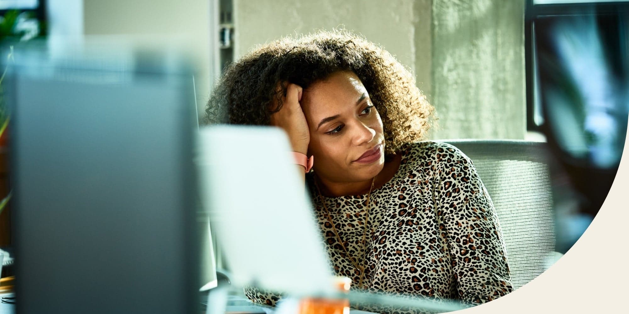 unhappy person sitting at office desk behind computer monitor and laptop looking off to the side